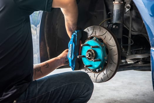 Bangkok, Thailand - February 4, 2023 : Unidentified car mechanic or serviceman disassembly and checking a disc brake and asbestos brake pads for fix and repair problem at car garage or repair shop