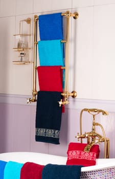 A vertical shot of colorful bamboo towels hanging on a golden rack in a bathroom