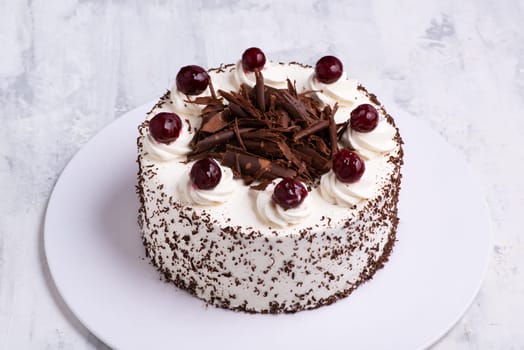 A closeup shot of white cream on Black Forest gateau cake with cherries on white marble surface