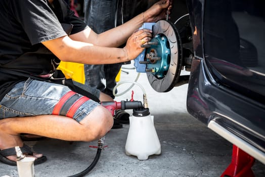 Bangkok, Thailand - March 6, 2021 : Unidentified car mechanic or serviceman disassembly and checking a disc brake and asbestos brake pads for fix and repair problem at car garage or repair shop