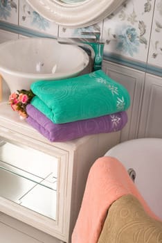 A vertical shot of folded turquoise, and purple bamboo towels and a pink towel near a bathroom sink