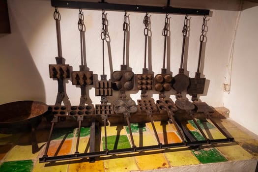 a wall in a bakery full of old metal waffle irons in various shapes such as round shell with and without rims that were formerly used to bake waffles