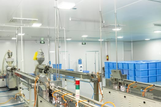 A factory of production of medical syringes and droppers, with equipment and blue containers in the background