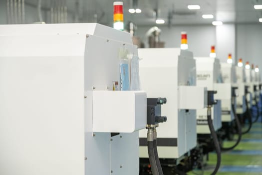 A selective focus of a molding machine from behind with hanging hosepipes in a factory for the production of medical syringes and droppers