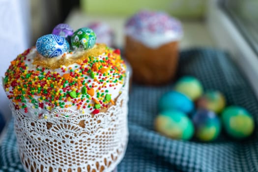 Three traditionally baked orthodox easter cakes with glace icing and bright blue and yellow flowers on wooden background with lace fabric and red candle. Easter kulich. Selective focus, copy space.