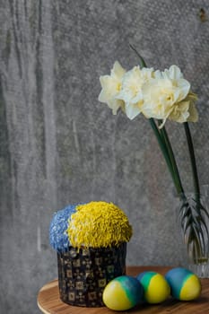 Delicious Easter cake in the colors of the flag of Ukraine, yellow-blue colored Easter eggs on a wooden table with flowers in the background. place for text. selective focus.