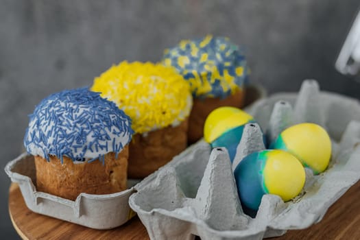 Easter cakes in the colors of the flag of Ukraine, yellow and blue in a cardboard stand with eggs, Easter eggs. place for text. selective focus.