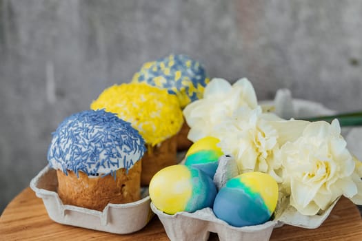 Easter cakes in the colors of the flag of Ukraine, yellow and blue in a cardboard stand with eggs, Easter eggs. place for text. selective focus.