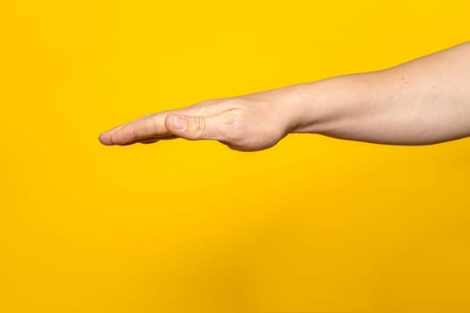 Strong man's arm with palm outstretched upside down isolated on yellow background