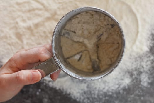 Flour is sifted through a sieve on the kitchen table