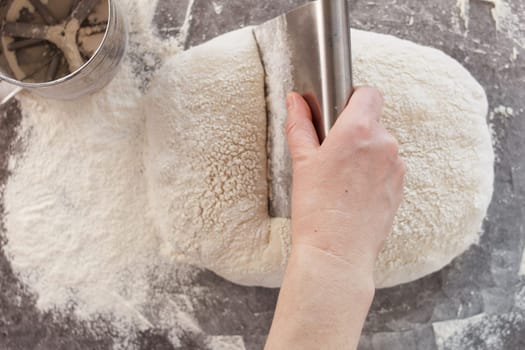 A woman's hand cuts the dough into pieces with a knife. Cooking bread, ciabatta.