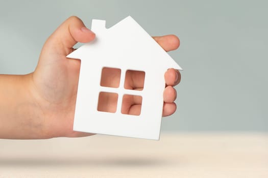 Real estate insurance. Model of a white house in hands on a gray blurred background. Insure a house or apartment, the concept of insurance services, with copy space.