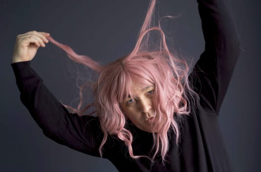 Portrait of a man who tried on a pink wig, looks at the camera, grimaces, poses. Close-up.