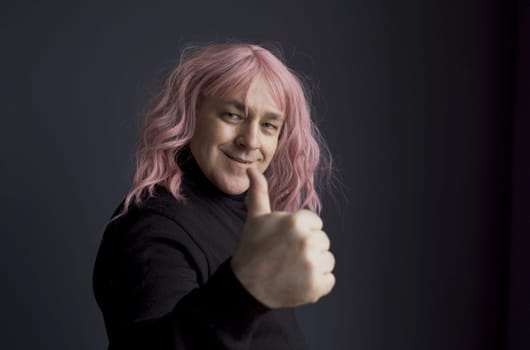 Positive man in a pink wig shows a hand gesture - thumbs up, great. Close-up.