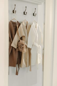 Three linen robes of different colors hang on a hanger in the bathroom. Vertical frame.