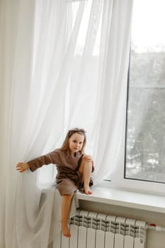 Portrait of a little girl in a brown dressing gown, who is sitting on the windowsill.