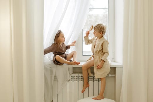 A boy and a girl are sitting on the windowsill in the bedroom, talking and playing.