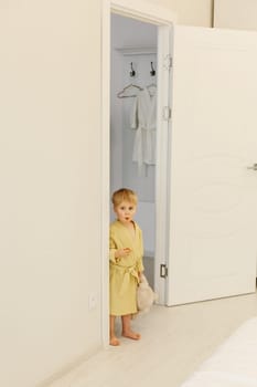 A small boy in a yellow bathrobe with a toy in his hands came out of the bathroom.