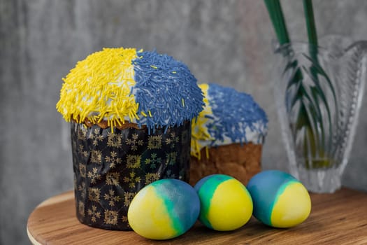 Delicious Easter cakes in the colors of the flag of Ukraine, yellow-blue colored Easter eggs on a wooden table with flowers in the background. place for text. selective focus.