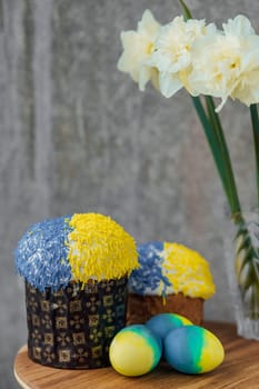 Delicious Easter cakes in the colors of the flag of Ukraine, yellow-blue colored Easter eggs on a wooden table with flowers in the background. place for text. selective focus