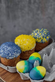 Easter cakes in the colors of the flag of Ukraine, yellow and blue in a cardboard stand with eggs, Easter eggs. place for text. selective focus.