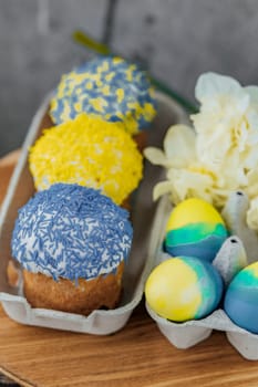 Easter cakes in the colors of the flag of Ukraine, yellow and blue in a cardboard stand with eggs, Easter eggs. place for text. selective focus.