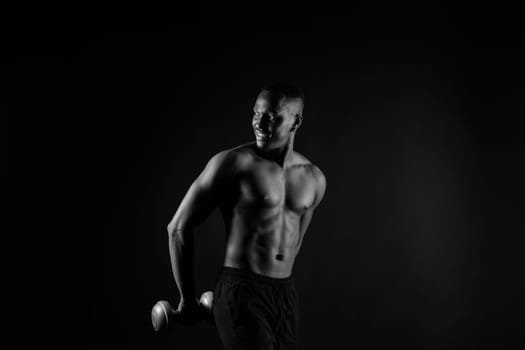 Isolated african muscular man with dumbbells on a dark studio background. Strong shirtless black guy