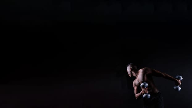 Isolated african muscular man with dumbbells on a dark studio background. Strong shirtless black guy