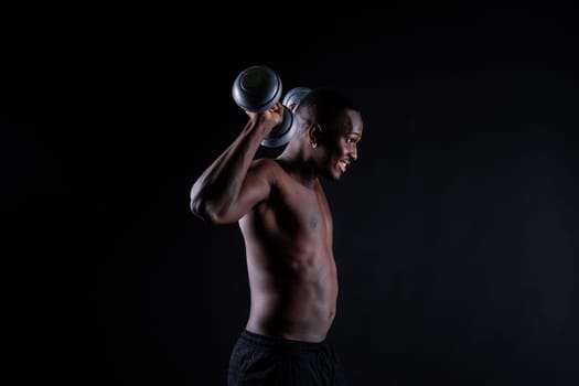 Isolated african muscular man with dumbbells on a dark studio background. Strong shirtless black guy