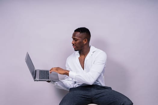 Optimistic african-american male student in a casual shirt using laptop pc isolated