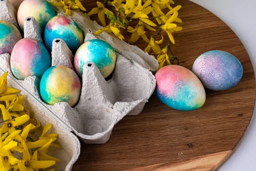 multi-colored Easter eggs on a wooden background, a green background next to yellow flowers.