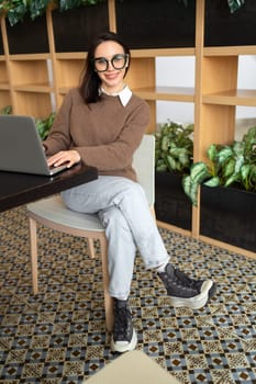 Woman Wearing Glasses using Laptop. Charming businesswoman in eyeglasses and casual clothes working with laptop computer looking at camera and smile. Elegant business female full length vertical shoot