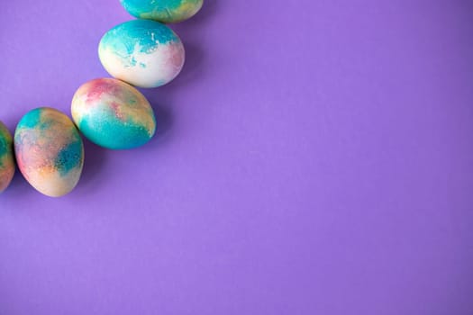 Easter composition with colorful eggs in shopping cart, wooden bunny and spring flowers on purple background. Easter frame of eggs painted in purple color. Copy space