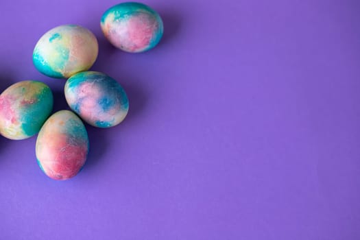 Easter composition with colorful eggs in shopping cart, wooden bunny and spring flowers on purple background. Easter frame of eggs painted in purple color. Copy space.