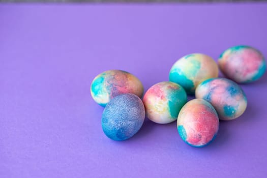 Easter composition with colorful eggs in shopping cart, wooden bunny and spring flowers on purple background. Easter frame of eggs painted in purple color. Copy space.