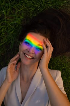 Top view of caucasian woman with rainbow ray on her face lies on green grass