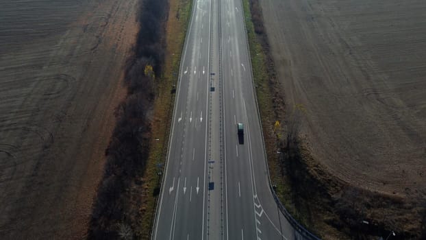 Cars driving along the highway on an autumn sunny day. Automobile road with white markings between agricultural fields. View of the cars driving on paved road. automobile vehicles. Aerial drone view.
