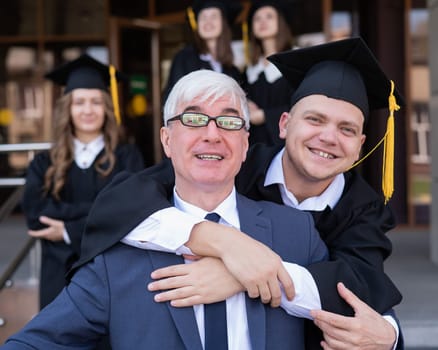 Father and son embrace at graduation. Parent congratulates university graduate