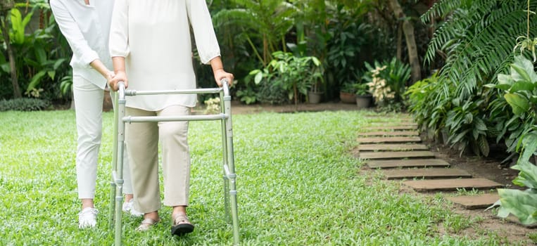 An old elderly Asian woman uses a walker and walking in the backyard with her daughter.  Concept of happy retirement With care from a caregiver and Savings and senior health insurance