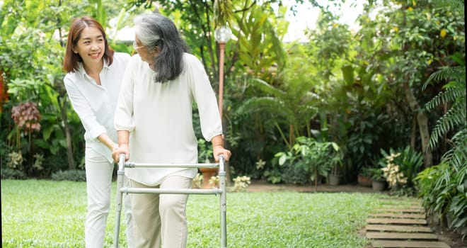 An old elderly Asian woman uses a walker and walking in the backyard with her daughter.  Concept of happy retirement With care from a caregiver and Savings and senior health insurance