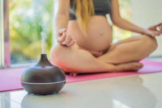Young pregnant woman doing yoga exercises and meditating at home with an aroma diffuser. Health care, mindfulness, relaxation and wellness concept. Aromatherapy during pregnancy.