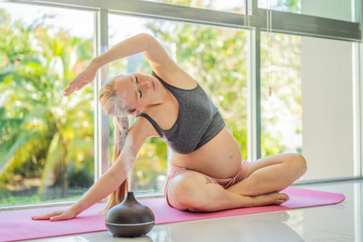 Young pregnant woman doing yoga exercises and meditating at home with an aroma diffuser. Health care, mindfulness, relaxation and wellness concept. Aromatherapy during pregnancy.
