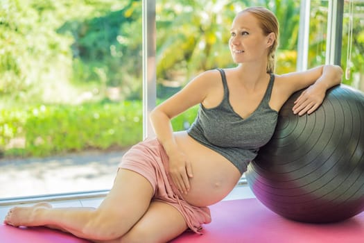 Pregnant woman exercising on fitball at home. Pregnant woman doing relax exercises with a fitness pilates ball. Against the background of the window.