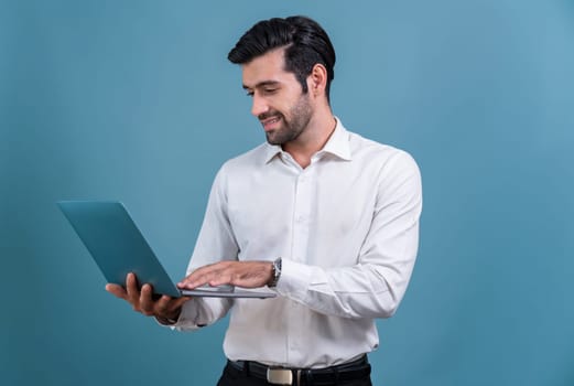 Successful businessman in black suit with innovative tech concept, standing pose and holding laptop and smiling with excitement on copyspace background for promotion or advertisement. Fervent