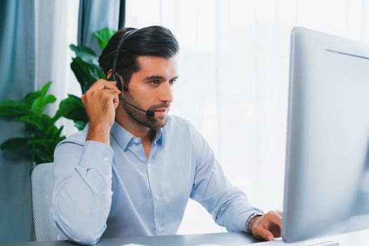 Male call center operator or telesales representative siting at his office desk wearing headset and engaged in conversation with client providing customer service support or making a sale. fervent