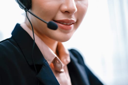 Asian call center with headset and microphone working on her workspace looking at camera. Female operator provide exceptional customer service. Supportive call center agent portrait. Enthusiastic