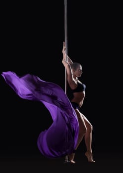 Young slim pole dancer posing with violet cloth, isolated on black