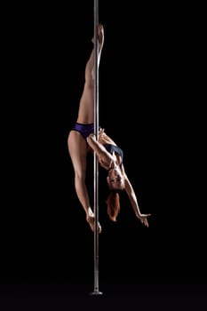 Young flexible woman dancing on pylon, isolated over black background