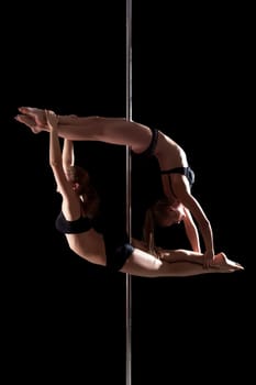 Duet of flexible young pole dancers, isolated on black