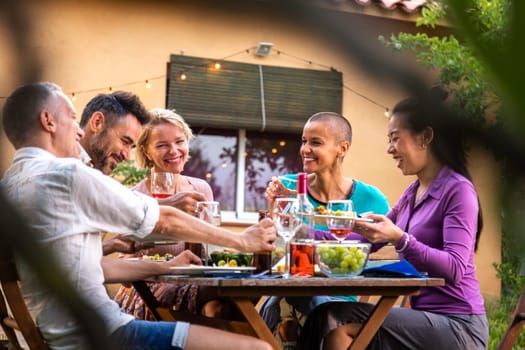 Happy group of friends laughing and eating during garden dinner party. Lifestyle.